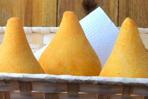 Coxinha in the basket, traditional Brazilian cuisine snacks stuffed with chicken, isolated on rustic wooden table photo