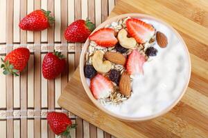 natural yogurt with homemade granola, strawberries and nuts in ceramic bowl on a table top view photo