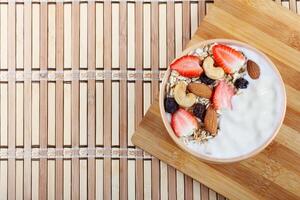 natural yogurt with homemade granola, strawberries and nuts in ceramic bowl on a table top view photo