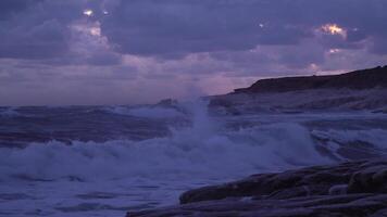 storm golven crashen rotsen kust. dramatisch luchten in de avond. 4k video