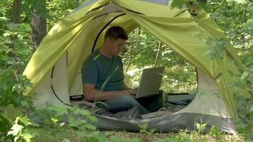 homme travaux derrière une portable dans une tente dans le forêt. pigiste éloigné travail concept. 4k video