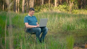 pazzo programmatore Lavorando su il computer portatile nel estate foresta a il soleggiato giorno. a distanza opera concetto. 4k video