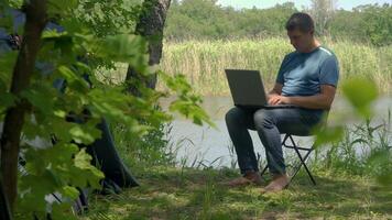 Mann funktioniert hinter ein Laptop in der Nähe in der Nähe von das Zelt im das Wald. er ist müde und will zu ausruhen. Freiberufler Fernbedienung Arbeit Konzept. 4k video