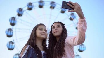 twee mooi jong vriendinnetjes maken een selfie Aan de achtergrond van een ferris wiel. 4k. detailopname video