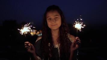 jovem lindo menina com grandes Sombrio cabelo detém fogos de artifício às noite e se alegra. lento movimento. video
