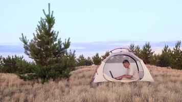 Man Works behind a Laptop in a tent. Freelancer Remote Work Concept. 4K video