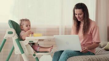 assistenza all'infanzia a casa, bambino protezione, nuovo vita, tempo libero con bambino. occupato mamma alimentazione bambino e Lavorando utilizzando il computer portatile video