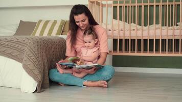 kinderopvang Bij huis, kind bescherming, nieuw leven, vrije tijd met baby. mam leest een boek naar de kind terwijl zittend in de buurt de bed video