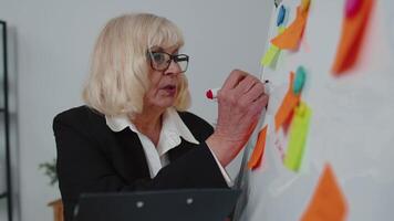 Elderly old business woman coach conference speaker analyzing infographics draw on office whiteboard video