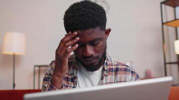 africano americano homem sentado em sofá abertura computador portátil pc iniciando trabalhos conectados dentro vivo quarto às casa video