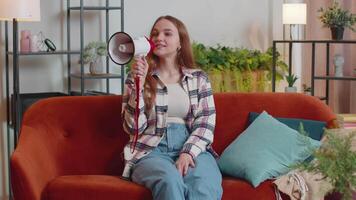 Young woman shout in megaphone loudspeaker announces discounts sale of real estate at home on sofa video