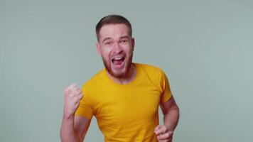 Stylish man in t-shirt shouting, raising fists in gesture I did it, celebrating success, winning video