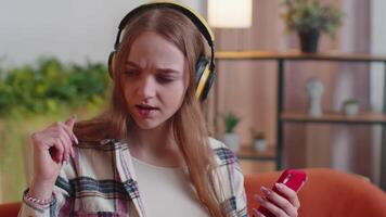 Pretty Caucasian young woman in headphones listening music dancing, singing in living room at home video