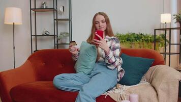 mulher sentado às casa usando crédito banco cartão e Smartphone enquanto transferindo dinheiro conectados compras video