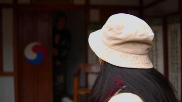 kvinna i förgrund med hatt ser mot en person stående i en traditionell dörröppning med koreanska flagga. video