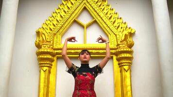 kvinna i röd klänning stående i främre av en traditionell gyllene tempel ingång. video