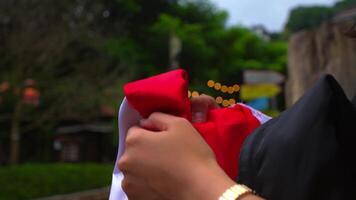 Close-up of a person's arm draped in a red fabric, with a gold watch on the wrist, against a blurred outdoor background. video