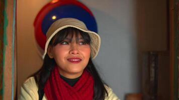 portrait de une souriant femme avec une chapeau et rouge écharpe à l'intérieur, chaud éclairage avec doux concentrer Contexte. video