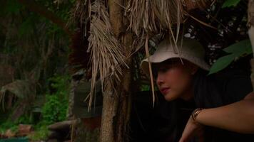 Person in a hat peeking out from behind tropical foliage in a jungle setting. video