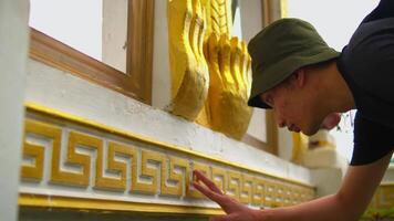 Craftsman touching up gold leaf on traditional temple architecture. video