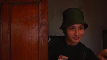 Portrait of a young man in a green bucket hat, smiling subtly indoors with a warm, dimly lit background. video