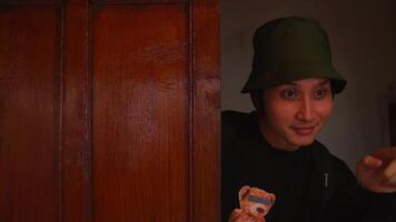 Portrait of a young man in a green bucket hat, smiling subtly indoors with a warm, dimly lit background. video