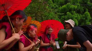 Group of women in traditional attire with red fans laughing and interacting with a person outdoors. video