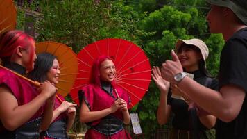 Group of women in traditional attire with red fans laughing and interacting with a person outdoors. video