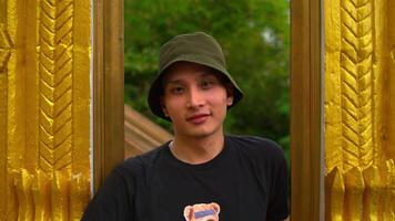 Man in black t-shirt and bucket hat posing in front of golden textured pillars. video