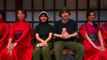 Group of young adults in traditional red attire sitting together with a smiling man in casual clothes at the center. video