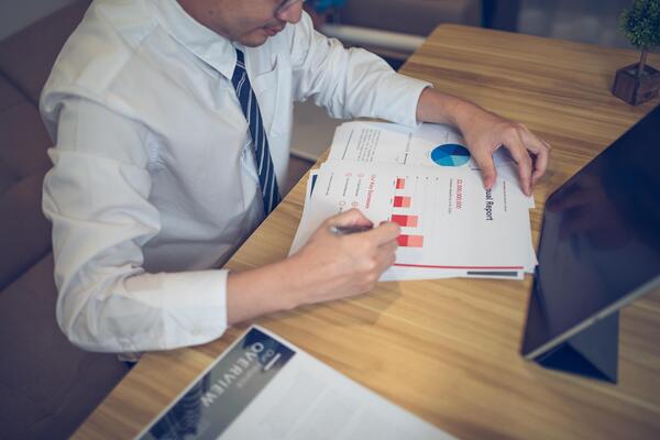 Businessman analyzing bar graph data with pen in hand, laptop and coffee on desk. Business concept