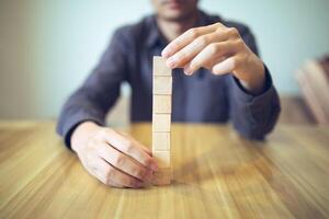 Hand strategically placing wooden blocks in a stair-step design on a table, signifying progressive success and growth photo