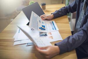 Businessman analyzing bar graph data with pen in hand, laptop and coffee on desk. Business concept photo