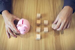 un persona con un cerdito banco y de madera bloques en un mesa, ilustrando conceptos de ahorros y inversión foto