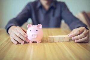 A person with a piggy bank and wooden blocks on a table, illustrating concepts of savings and investment photo