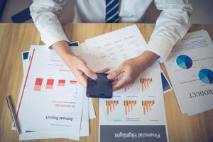 Business professional engaging with smartphone among various financial documents on a desk photo