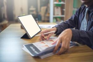 Businessman analyzing statistics on documents with a mock-up screen laptop at a workspace photo