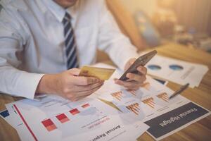 Businessperson holding a credit card and smartphone amid financial papers. E-commerce business concept photo