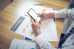 Businessman analyst using smartphone with screen mockup over financial charts for data management and analysis photo