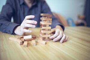 Business strategy concept with hands playing a wooden block tower game, symbolizing risk and stability. Planning risk management photo