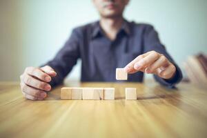 Hand strategically placing wooden blocks in a stair-step design on a table, signifying progressive success and growth photo