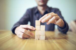 Hand strategically placing wooden blocks in a stair-step design on a table, signifying progressive success and growth photo