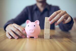 Person building a tower from wooden blocks beside a piggy bank, symbolizing financial planning and saving photo