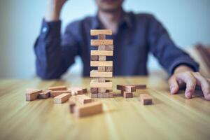 Business strategy concept with hands playing a wooden block tower game, symbolizing risk and stability. Planning risk management photo