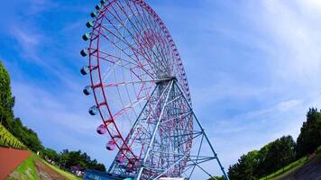 A timelapse of moving ferris wheel at the park behind the blue sky fish-eye shot tilt video