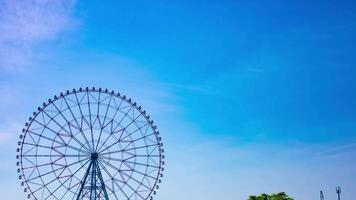 A timelapse of moving ferris wheel at the park behind the blue sky wide shot panning video