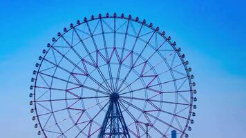 A timelapse of moving ferris wheel at the park behind the blue sky panning video