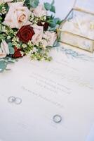 Wedding rings lie on the marriage certificate on the table near the bouquet of flowers photo