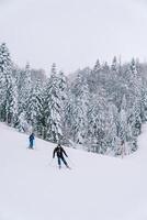 Skiers in ski suits go down a snow-covered slope photo