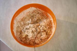 Spoon sharpens from a bowl with kneaded dough on the table. Top view photo